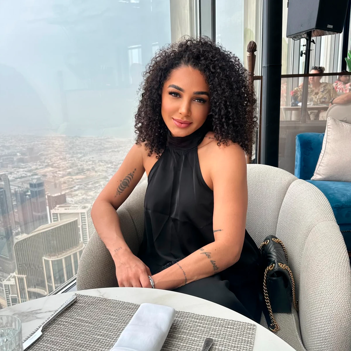 Larissa seated beside a panoramic Dubai skyline view